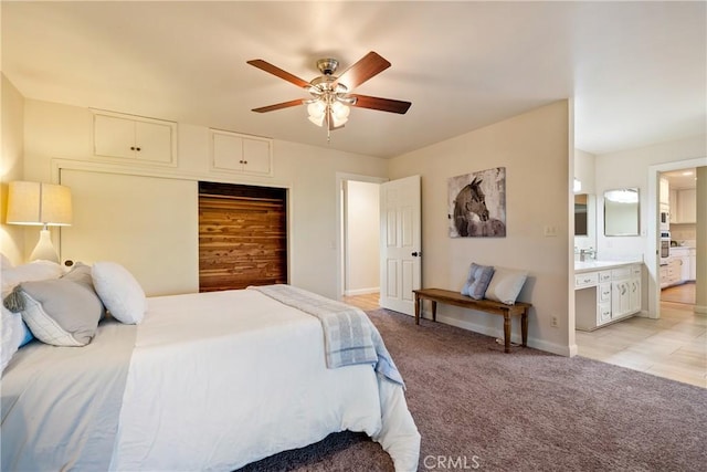 bedroom featuring light carpet, ceiling fan, baseboards, and ensuite bath