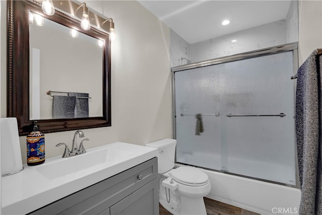 full bathroom featuring wood-type flooring, shower / bath combination with glass door, vanity, and toilet