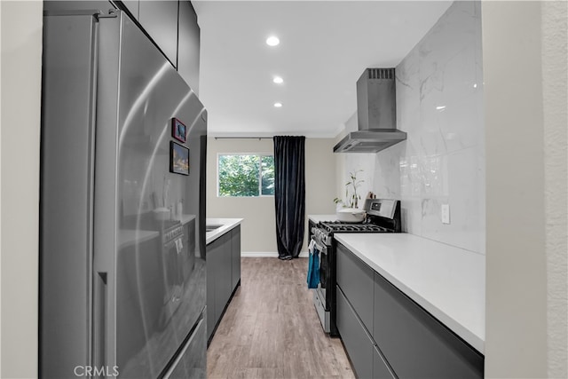 kitchen featuring appliances with stainless steel finishes, wall chimney exhaust hood, light wood-type flooring, and decorative backsplash