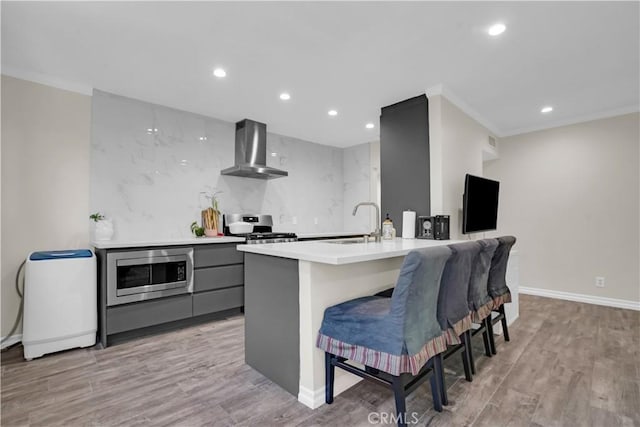 kitchen with a sink, gray cabinetry, light countertops, stainless steel appliances, and wall chimney range hood