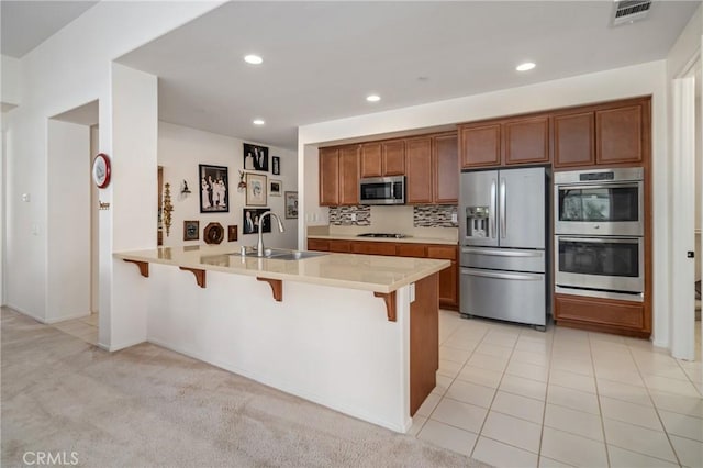 kitchen featuring light carpet, appliances with stainless steel finishes, kitchen peninsula, a kitchen breakfast bar, and sink