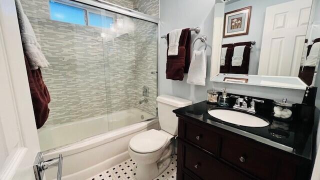 full bathroom featuring tile patterned flooring, bath / shower combo with glass door, toilet, and vanity