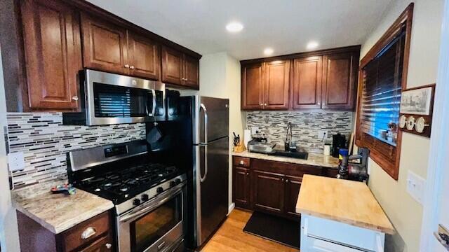 kitchen featuring dark brown cabinetry, butcher block countertops, backsplash, stainless steel appliances, and light hardwood / wood-style floors