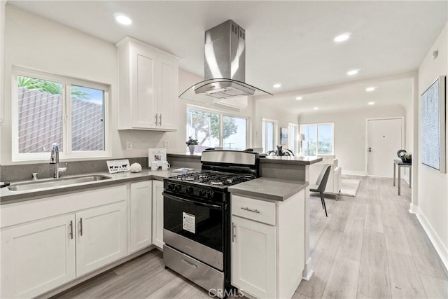 kitchen featuring wall chimney exhaust hood, sink, stainless steel gas range, a wealth of natural light, and white cabinetry