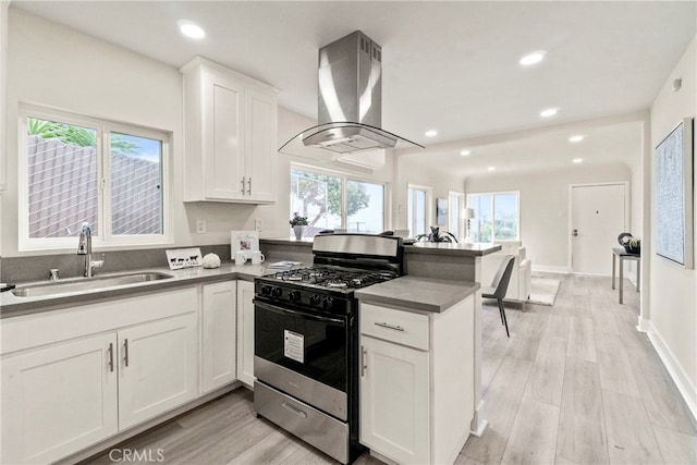 kitchen featuring plenty of natural light, wall chimney range hood, gas stove, sink, and white cabinets