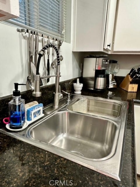 room details featuring white cabinets, dark stone counters, and sink