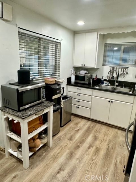 kitchen with light wood-type flooring, white cabinetry, and sink