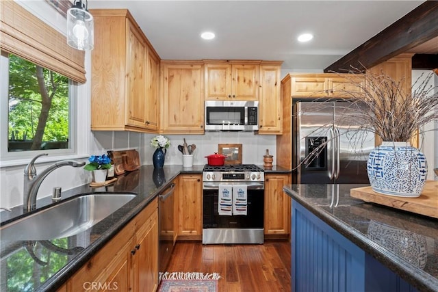 kitchen with appliances with stainless steel finishes, dark wood-type flooring, hanging light fixtures, dark stone counters, and sink