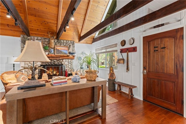 interior space with dark hardwood / wood-style flooring, a stone fireplace, rail lighting, lofted ceiling with beams, and wooden ceiling