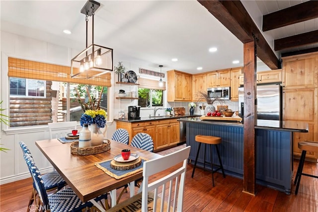 kitchen with a kitchen bar, beamed ceiling, hanging light fixtures, appliances with stainless steel finishes, and dark wood-type flooring