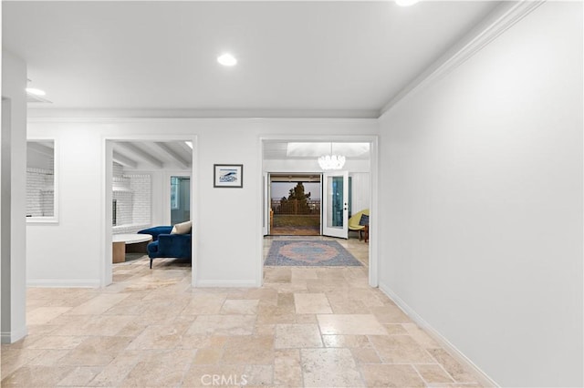 hall featuring a notable chandelier, stone tile floors, baseboards, and crown molding