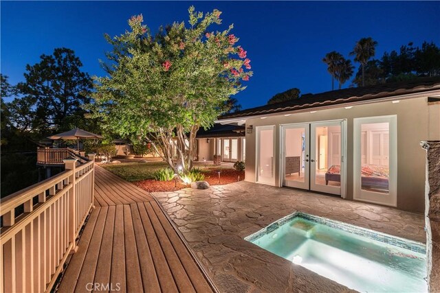 deck at twilight with french doors, a patio area, and a jacuzzi