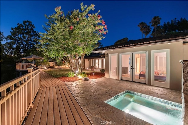 deck at night with french doors, a patio area, and a jacuzzi