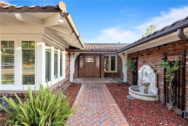 view of exterior entry with a tiled roof and brick siding