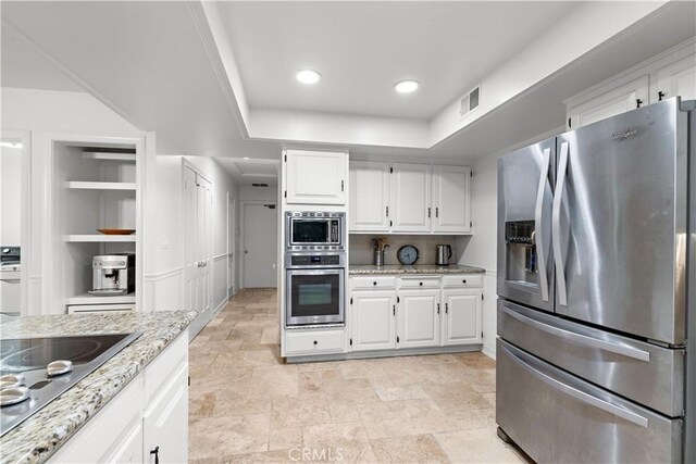 kitchen with white cabinetry, stainless steel appliances, a raised ceiling, and light stone counters