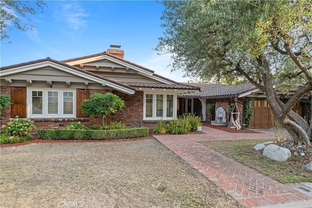 ranch-style home featuring a tiled roof, brick siding, and a chimney