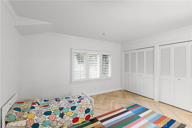 unfurnished bedroom with light parquet flooring, ornamental molding, and multiple closets