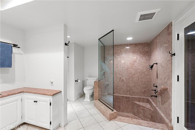 bathroom with toilet, tile patterned flooring, and a tile shower