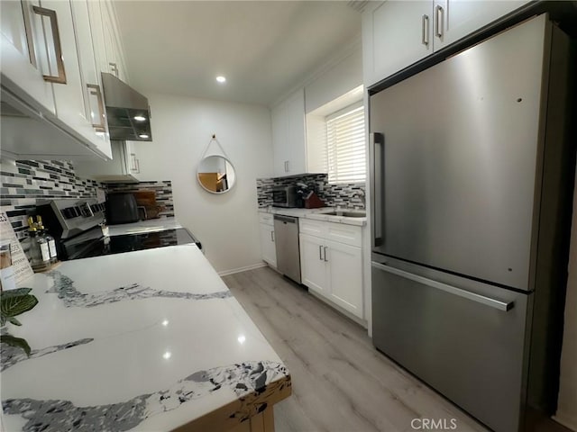 kitchen featuring light hardwood / wood-style flooring, white cabinetry, stainless steel appliances, ventilation hood, and light stone countertops