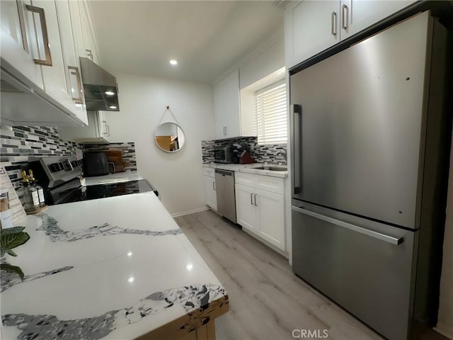 kitchen with light wood-style flooring, appliances with stainless steel finishes, light stone countertops, extractor fan, and white cabinetry