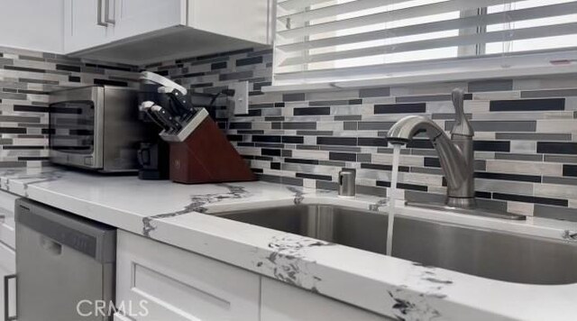 kitchen featuring white cabinetry, decorative backsplash, and stainless steel dishwasher