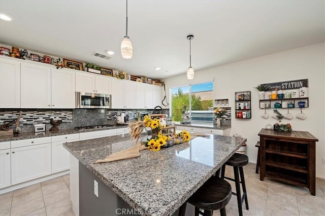 kitchen with pendant lighting, a center island with sink, stainless steel appliances, and stone countertops