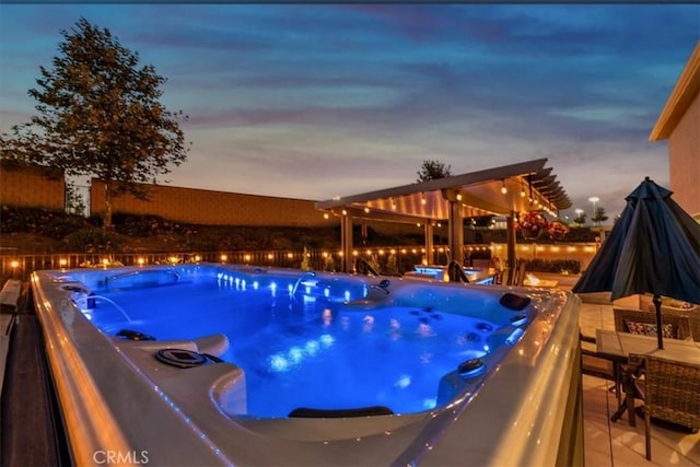 pool at dusk with a hot tub