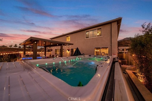 pool at dusk featuring a hot tub