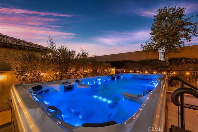 pool at dusk featuring a hot tub