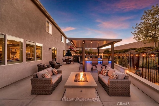 patio terrace at dusk featuring exterior bar and an outdoor living space with a fire pit