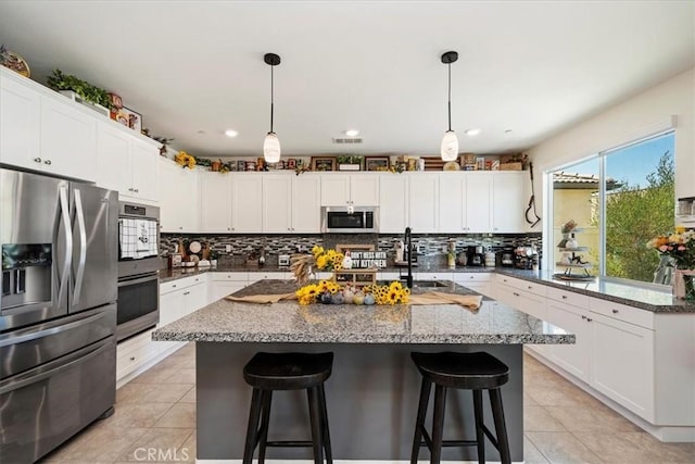 kitchen featuring white cabinetry, dark stone countertops, decorative light fixtures, a center island with sink, and appliances with stainless steel finishes