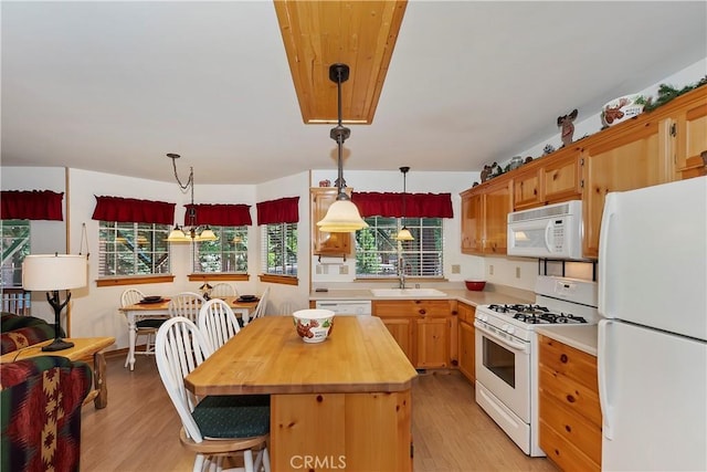 kitchen with sink, a center island, hanging light fixtures, white appliances, and light wood-type flooring