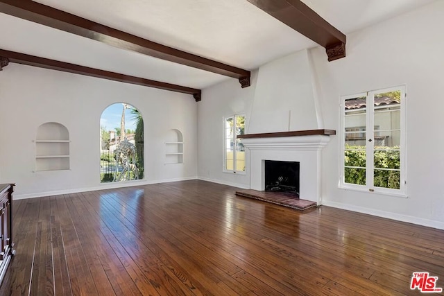 unfurnished living room with beam ceiling, a large fireplace, dark hardwood / wood-style floors, and plenty of natural light