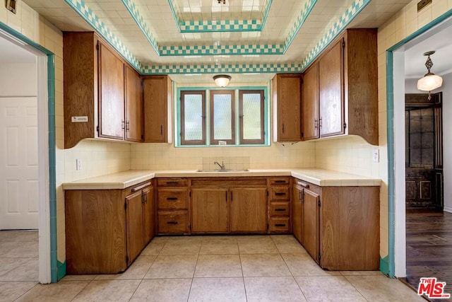 kitchen featuring tile countertops, sink, decorative backsplash, light tile patterned floors, and a tray ceiling