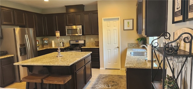 kitchen featuring appliances with stainless steel finishes, light stone countertops, a kitchen island, and sink