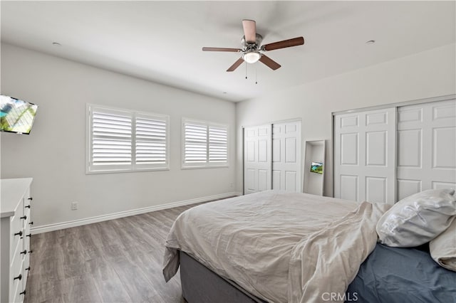 bedroom with multiple closets, light hardwood / wood-style floors, and ceiling fan