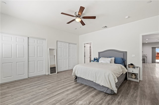 bedroom featuring light hardwood / wood-style flooring, two closets, and ceiling fan