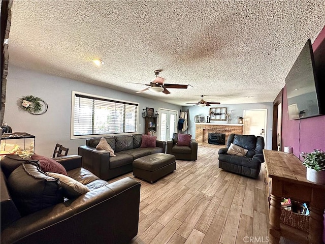 living room with ceiling fan, a textured ceiling, a brick fireplace, and light wood-type flooring