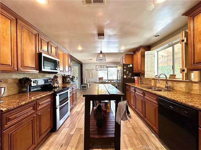 kitchen with decorative backsplash, sink, hanging light fixtures, light stone countertops, and stainless steel appliances