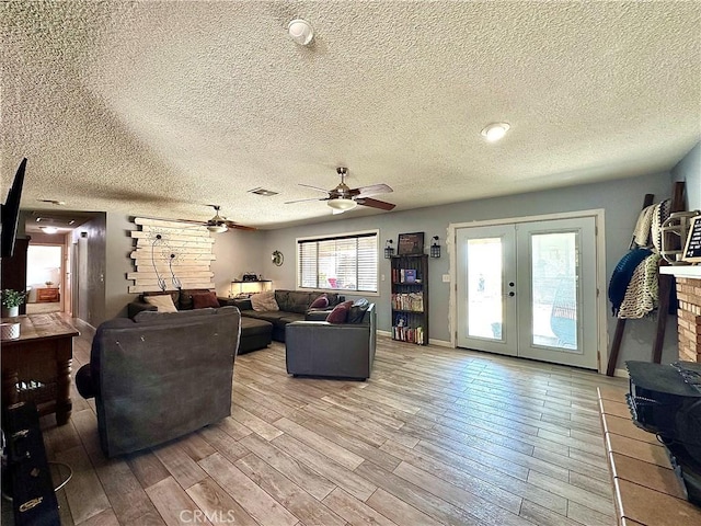 living room featuring a textured ceiling, ceiling fan, light hardwood / wood-style floors, and french doors