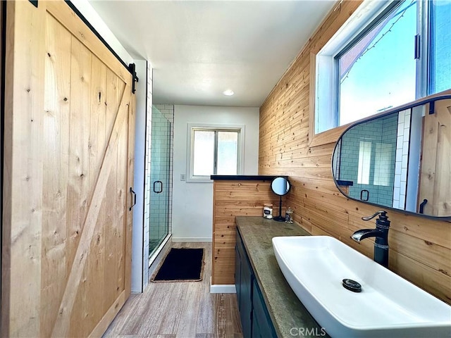 bathroom featuring a shower with shower door, hardwood / wood-style flooring, vanity, and wood walls