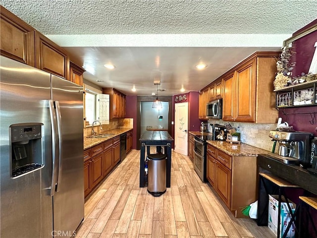 kitchen featuring stainless steel appliances, light wood-type flooring, a kitchen island, pendant lighting, and sink