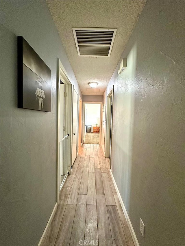 corridor featuring light wood-type flooring and a textured ceiling