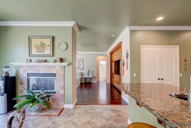 interior space featuring light hardwood / wood-style floors, a textured ceiling, stone counters, a fireplace, and ornamental molding