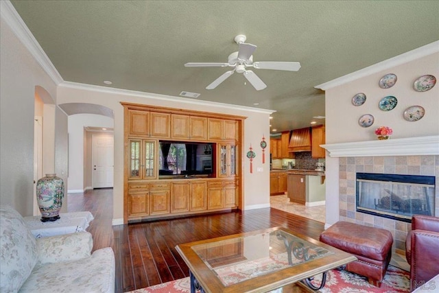 living room with ceiling fan, crown molding, a fireplace, and dark hardwood / wood-style flooring