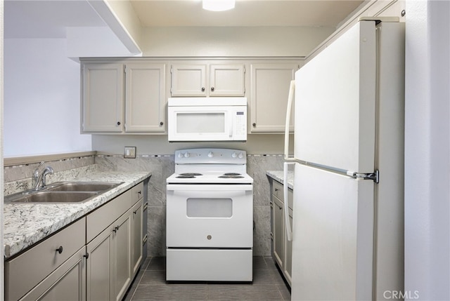 kitchen with dark tile patterned floors, white appliances, light stone countertops, and sink