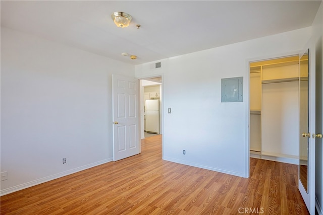 unfurnished bedroom with a closet, light hardwood / wood-style floors, electric panel, and white fridge