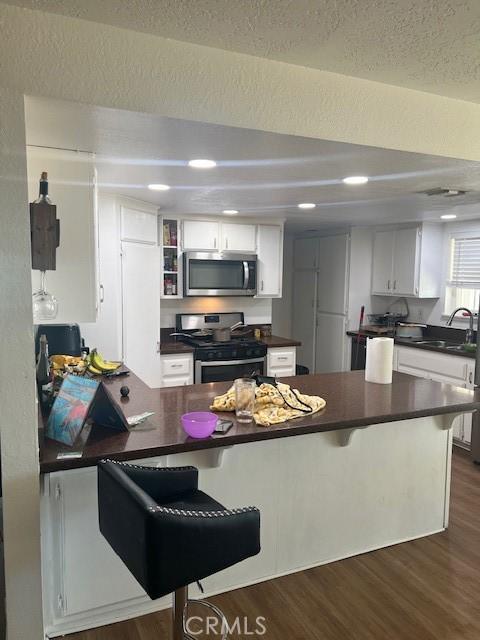 kitchen featuring sink, appliances with stainless steel finishes, white cabinetry, a kitchen breakfast bar, and kitchen peninsula