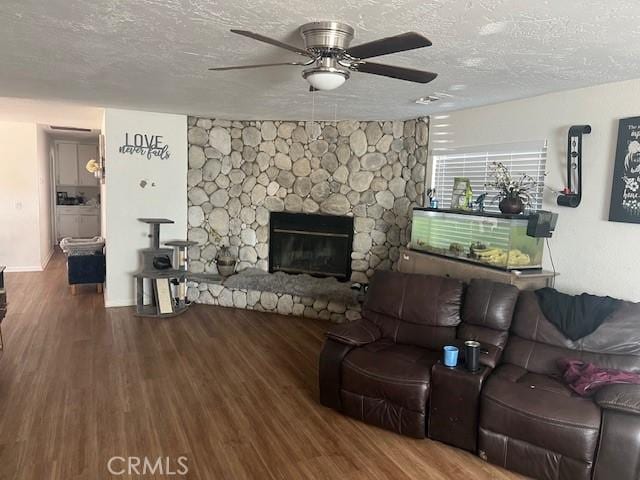 living room featuring hardwood / wood-style floors, a stone fireplace, a textured ceiling, and ceiling fan