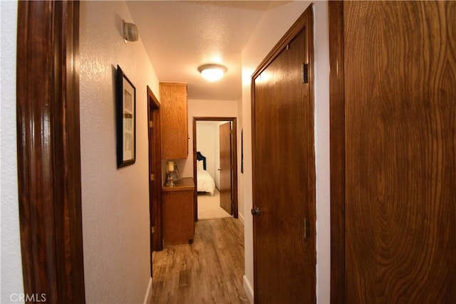 corridor with light wood-type flooring and a textured ceiling